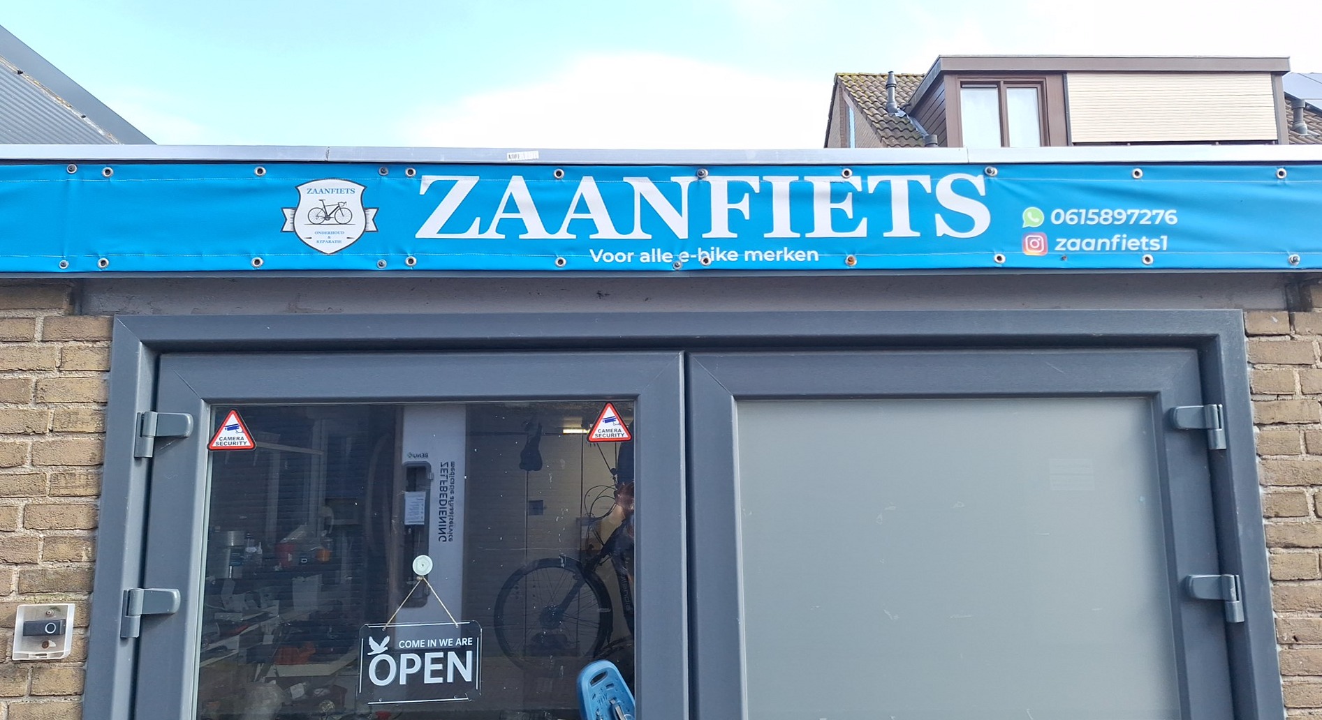 De gevel van Zaanfiets met de blauwe banner met de naam, het telefoonnummer en het Instagram-account