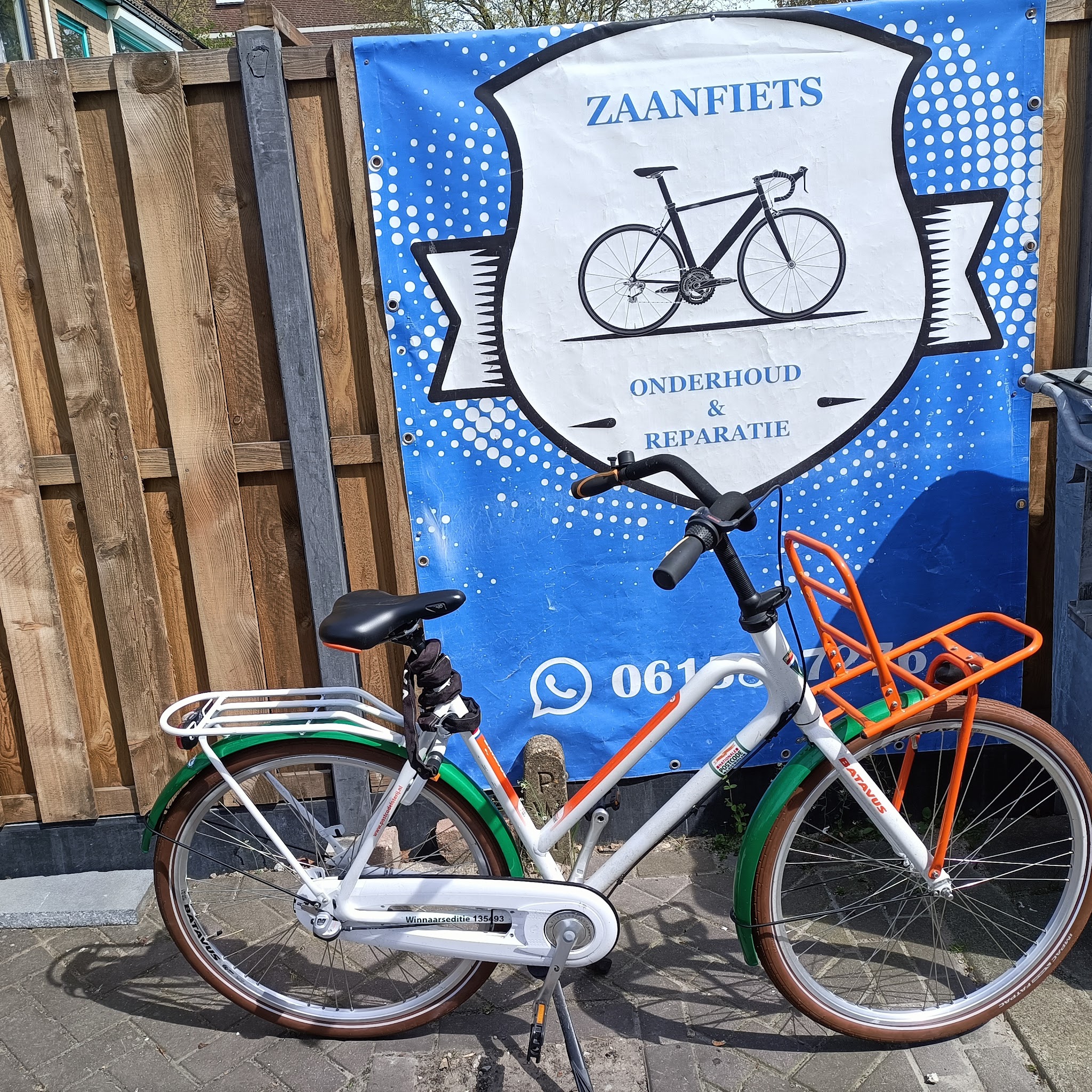 Een witte stadsfiets met groene spatborden voor het Zaanfiets-spandoek